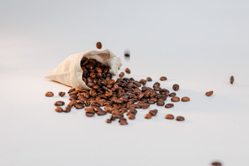 Coffee beans pouring out of a bag onto a clean white surface.
