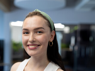 Young woman smiling in office, light green headband and gold hoop earrings, copyspace