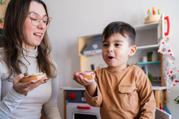 Happy toddler boy and mother playing with wooden toy food in play kitchen