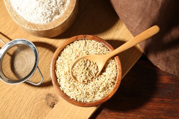Brown rice, flour and sieve on wooden table, flat lay