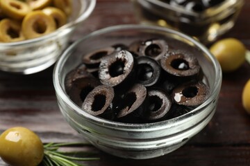 Delicious marinated olive rings, whole one and rosemary on wooden table, closeup