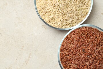 Different types of brown rice in glass bowls on light grey table, top view. Space for text