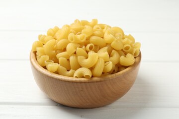 Raw horns pasta in bowl on white wooden table, closeup