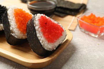 Tasty tobiko onigiri (Japanese rice balls) served on light grey table, closeup. Space for text
