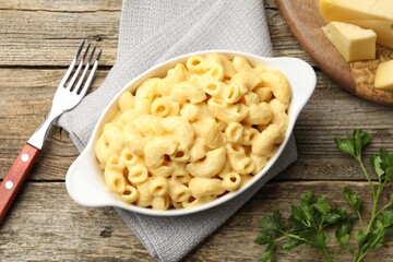 Delicious pasta with cheese sauce, parsley and fork on wooden table, flat lay