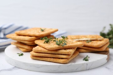 Tasty salty crackers with thyme on white marble table, closeup
