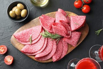 Slices of delicious sausage with rosemary served on black table, flat lay
