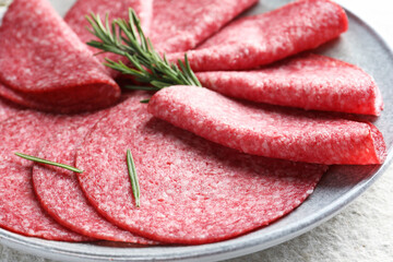 Slices of delicious sausage with rosemary served on white textured table, closeup