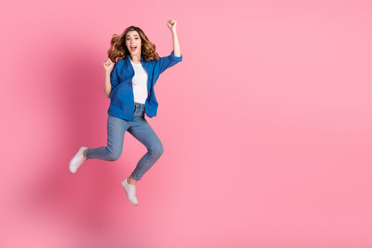 Young woman jumping joyfully with a vibrant smile, wearing stylish casual attire, posing against a vibrant pink backdrop