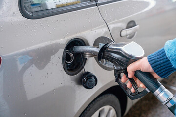 Fueling a car at a gas station on a rainy day with a focus on the pump and vehicle during the...
