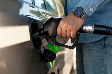 Man fueling car at  gas station during daytime with bright sunlight highlighting the activity and...
