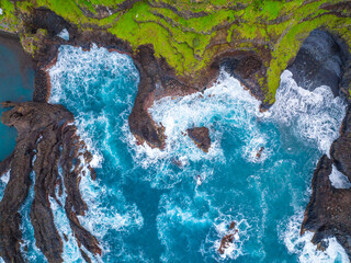Waves crashing against rocky coastline with lush green cliffs in daylight