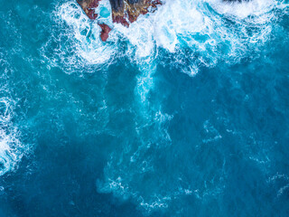Waves crash on rocky shore under clear blue sky at midday