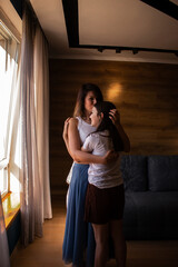 Adoptive mother holds her daughter close standing near window showing connection and warmth. Concept of modern family and power of love beyond biology. Vertical.