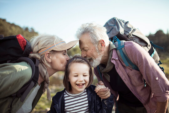 Happy grandparents kissing granddaughter during outdoor hiking trip