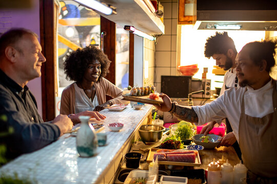 Chefs serving sushi to smiling customers at Japanese restaurant counter