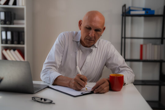 Asian engineer wearing a safety vest, pointing at a blueprint on the table while engaging in a discussion about a building project with businesswomen in the modern office setting