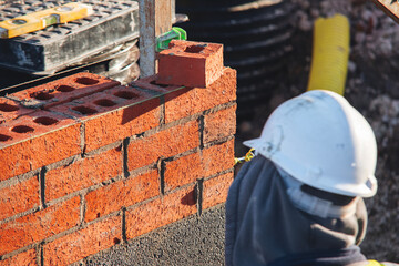 Bricklayer laying bricks at building site in bright sunlight