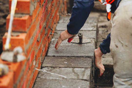 Mason laying concrete blocks while constructing retaining wall at construction site
