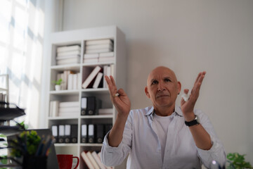 Senior businessman sitting at a desk and gesturing animatedly during a video call, surrounded by bright office decor and bookshelves, showcasing effective communication in a remote work setting