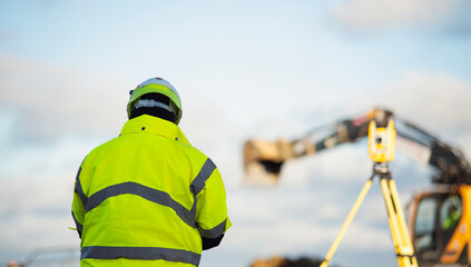 Land surveyor in bright safety gear overseeing heavy machinery on construction site
