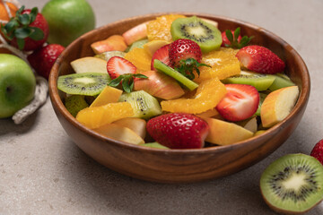 Fruit salad in wooden bowl on beige background. Kiwi, orange, strawberry, apple, pear side view