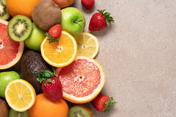 Set of fruits and berries top view on beige background with copy space. Orange, grapefruit, avocado, lemon, kiwi, apple, pear and ripe strawberry