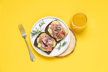 Smoked salmon avocado sandwich on yellow background. Black whole grain bread, avocado, salted salmon and dill for healthy breakfast