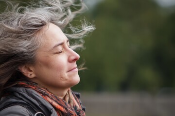 A woman's profile in the wind, with hair blowing back, eyes closed, in a moment of peace.