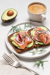 Smoked salmon avocado sandwich on light background. Black whole grain bread, avocado, salted salmon and dill for healthy breakfast