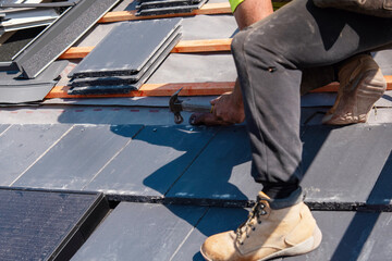 Skilled roofer installs slate roofing tiles at construction site