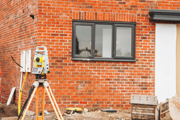 Construction site features surveying equipment set against newly built brick wall 