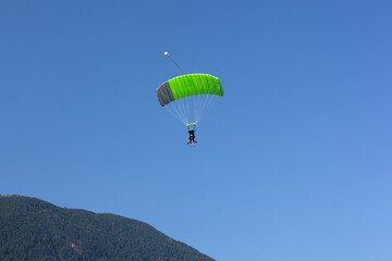 A paraglider with a green parachute is descending down to Kanin, Slovenia,