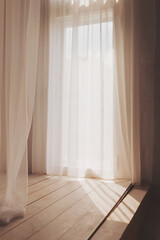 Soft sunlight filters through sheer curtains, casting gentle shadows on a serene wooden floor in a...