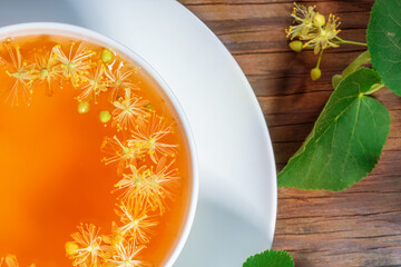 Linden tea with linden flowers in a white cup on a wooden background. View from above.