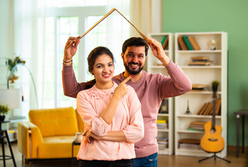 Indian Asian Husband playfully forms cardboard roof over wife's head, symbolizing their dream home
