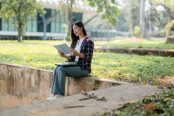 Young female student reading textbook, sitting outdoors on grass, surrounded by campus greenery during study session