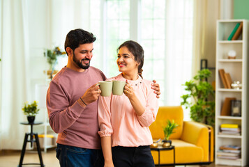 Happy Indian pair shares joyful moment sipping hot beverage and eating biscuits indoors