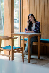 Young woman sitting at cafe table, smiling while texting on smartphone, enjoying relaxed moment during casual communication