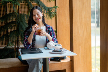 Female student sipping cold beverage while resting between classes, relaxing in bright campus coffee shop with laptop and books nearby
