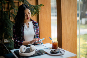 Young Asian student using calculator while studying at a table in a cafe with iced coffee and...