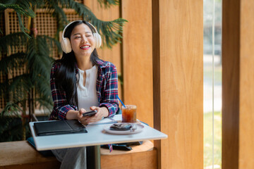 Young woman enjoying music and using mobile phone while sitting at a table in a cafe, with iced coffee and a chocolate donut