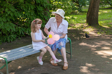 Grandmother and granddaughter sitting on a bench in a garden. Happy family moment with two people, an elderly woman and a young baby girl, enjoying time together outdoors
