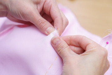 Hands carefully sewing pink fabric with needle and thread on a wooden table during a crafting session in daylight