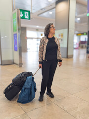 Senior woman waiting at the airport with luggage and jacket