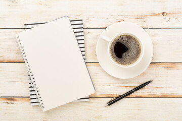 Notebook with cup of coffee on wooden background, top view