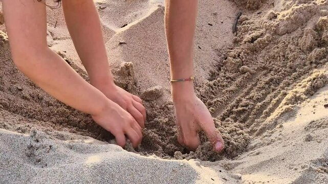Two children dig holes in the warm beach sand on a sunny afternoon, using their hands and imagination to create playful shapes in a moment of creative and carefree summer fun.