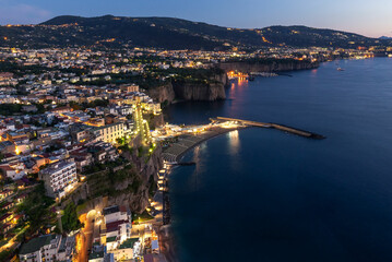 Blue hour view of the Sorrento Coast, Italy, with the city lights glowing against the twilight sky. The coastline, perched above the Mediterranean Sea