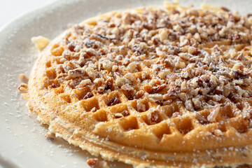 A closeup view of a waffle, topped with chopped pecan and powdered sugar, as a background.