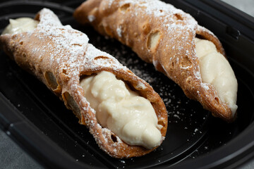 A view of two cannolis in a plastic container.